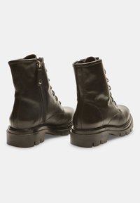 Stivaletti neri in pelle con una texture liscia, chiusura con lacci sul davanti, zip sul retro e suole in gomma spesse. Presentano una punta rotonda e accenti minimali.