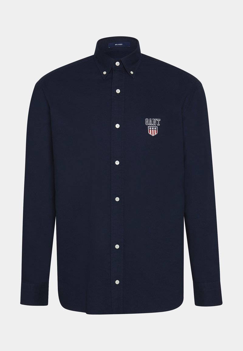 Camicia azzurra in cotone con bottoni, colletto classico, bottoni bianchi e logo GANT ricamato con design a scudo sul lato sinistro del petto.