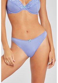 Lavender Slip mit glatter Oberfläche, zarter Spitzenkante und einem kleinen türkisfarbenen Schleifenakzent in der Mitte vorne.