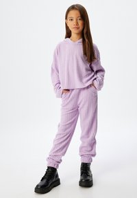 Conjunto de loungewear morado de forro polar que incluye una sudadera con capucha de textura acanalada y pantalones a juego, combinados con botas de combate negras.