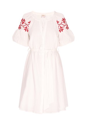 Vestido blanco con mangas abullonadas y patrones bordados en rojo en los hombros. Presenta una cintura con cordón y detalle de borlas.