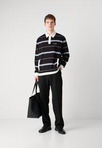 Čierno-biele pruhované polo tričko s dlhým rukávom a s golierom, skombinované s čiernymi nohavicami a čiernou taškou. Look dopĺňajú neformálne topánky.