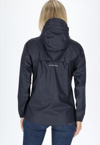 Navy waterproof jacket featuring a hood, elastic cuffs, and a badge detail at the back. Smooth, shiny fabric with a relaxed fit.