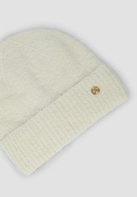 Gorro de punto color crema con un puño acanalado doblado y un pequeño logo dorado. Textura suave y diseño de cima redondeada.