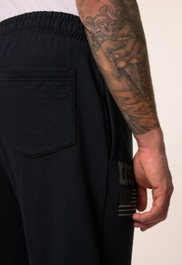 Marineblauwe joggingsbroeken met een elastische tailleband, een achterzak met een gegraveerd logo en een patch met "US" en een ontwerp van de Amerikaanse vlag.