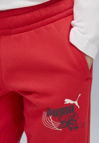 Pantaloni della tuta rossi in misto cotone, con logo PUMA nero e design grafico. Vita elastica con tasche laterali, texture liscia.