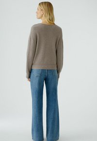 Pull en maille côtelée marron clair avec une coupe décontractée, associé à un jean bleu à jambe large avec des détails subtils sur les poches.