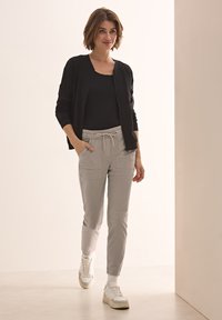 Svart zip-up cardigan, grå drawstring-byxor med sidofickor och vita sneakers; slät tyg, avslappnad passform och neutrala toner.