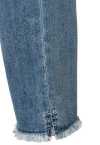 Close-up van een blauwe spijkerbroekspijp met een rafelige zoom en een detail met een zijsplit.