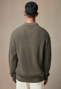 Kullgrøn strikket sweater, ribbet tekstur, lange ærmer, afslappet pasform, rund halsudskæring, med subtile sømdetaljer ved skuldrene.