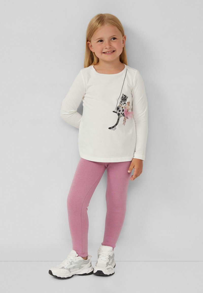 Weißes Langarmshirt mit einer Katzenillustration und einem rosa Tüllrock, kombiniert mit hellrosa Leggings und weißen Turnschuhen mit silbernen Akzenten.