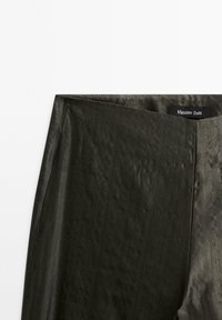 Jupe vert olive foncé avec un léger éclat et un détail de couture diagonale près de la taille, étiquetée Massimo Dutti.