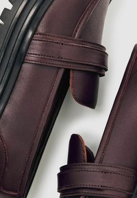 Pruunid nahast kingad, millel on ühtlane disain, ümar kuju ja Velcro rihmad. Tekstuuriga pind ning kontrastne must kummitald.