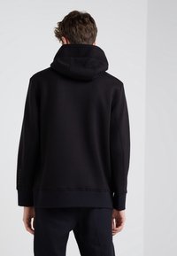 Svart hoodies med avslappnad passform, ribbad mudd och nederkant. Tyget är slätt med synliga sömmar och en märkesdetalj på ärmen.