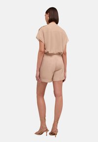 Beige kortärmad jumpsuit med en avslappnad passform, med krage och tygskärp. Matchad med nude klackar med remmar.