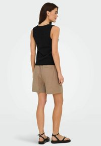 Top negro sin mangas con un acabado texturizado, combinado con pantalones cortos marrón claro con un patrón de cuadros y un bolsillo trasero, llevados con sandalias negras.