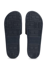 Tamsiai mėlynos gumos sandalų padai su tekstūruotu raštu, kuriame yra kvadratinių ir stačiakampių akcentų. Išgraviruotas "TOMMY HILFIGER" logotipo detalė.