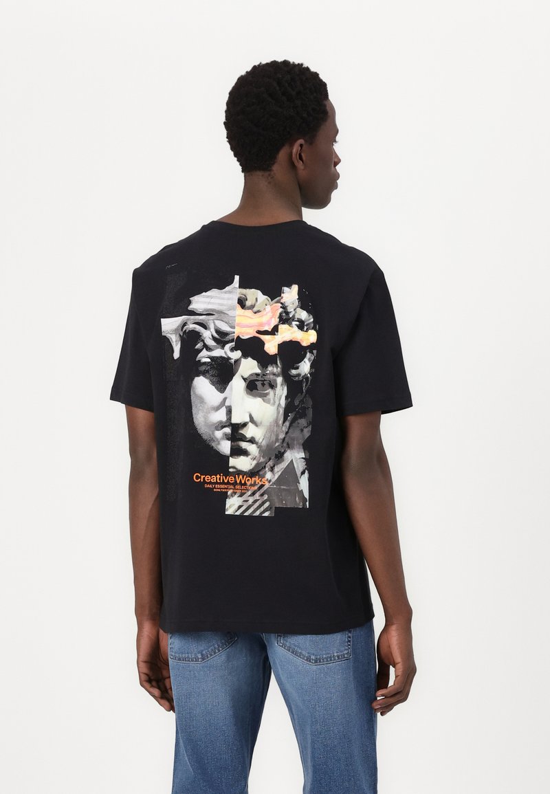 Sort bomulds t-shirt med et grafisk design af klassiske skulpturer og teksten "Creative Works" i orange. Korte ærmer og afslappet pasform.