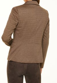 Hnědý houndstooth saka s přizpůsobeným střihem, s klopami a zapínáním na jeden knoflík. Obsahuje hladkou látku a úzké rukávy.