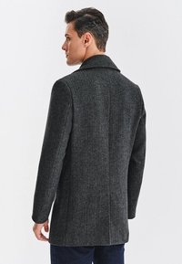 Szary wełniany płaszcz w jodełkę z klapami, długimi rękawami i dopasowanym krojem. Gładka faktura z wyraźną sylwetką.