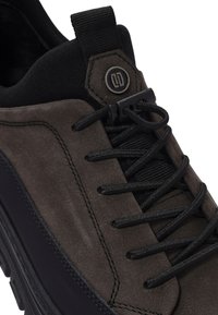 Baskets gris foncé avec une tige en daim et synthétique, dotées de lacets noirs, d'une languette noire et d'un accent en métal sur le côté.