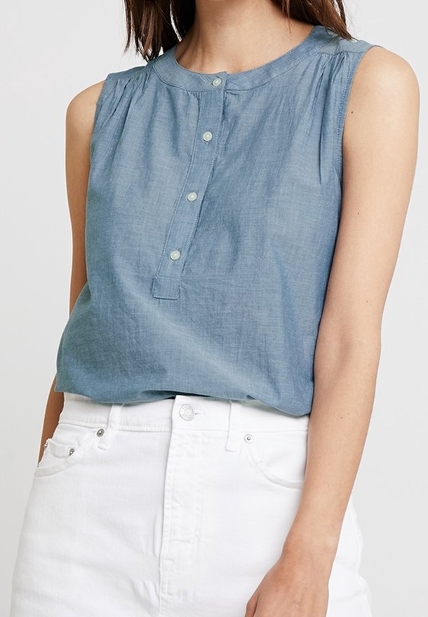 Chemise sans manches bleu clair en tissu doux, avec un col rond, une patte de boutonnage et un plissage discret le long des épaules.