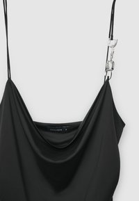 Schwarzes ärmelloses Kleid mit einem drapierten Ausschnitt. Verfügt über dünne Träger und silberne Beschläge an einem Träger. Der Stoff wirkt glatt und weich.