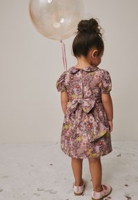 Vestido floral morado con mangas cortas abullonadas, cuello y un lazo en la parte trasera. Completado con zapatos rosa claro y un globo transparente.