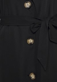 Black coat made of smooth fabric, featuring large circular buttons in shades of gold and brown, with a tied belt and a sleek silhouette.