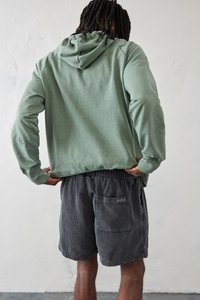 Grøn bomulds hoodie med kængurulomme, parret med mørke kordfløjl shorts med elastisk talje og baglomme.