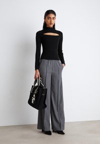 Top in maglia nera a coste con dettaglio cut-out, abbinato a pantaloni grigi a gamba larga. Accessoriato con una borsa nera con stampa grafica.