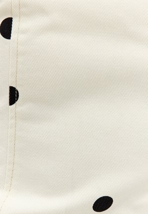 Tissu blanc avec une couture diagonale et de grands pois noirs partiellement visibles le long des bords.