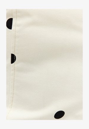 Tissu blanc avec une couture diagonale et de grands pois noirs partiellement visibles le long des bords.