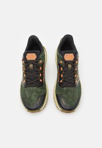 Green and black athletic shoes with a textured upper, orange accents, and patterned laces. Features a cushioned sole and branded detail.