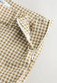 Tissu à carreaux marron et blanc avec une fermeture éclair latérale, une fermeture à bouton, et une légère brillance, doté d'une ceinture unie et d'une texture douce.