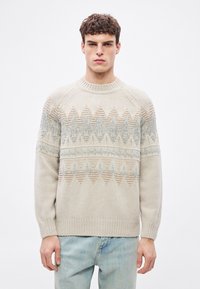 Beżowy sweter dziergany z okrągłym dekoltem, ozdobiony geometrycznymi wzorami w odcieniach jasnoniebieskiego i brązowego na wysokości klatki piersiowej i na rękawach.