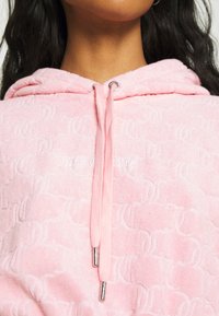 Rosa Kapuzenpullover mit strukturierter Stoffqualität, geprägt mit Buchstabenmuster und silberfarbenen Beschlägen am Kordelzug.