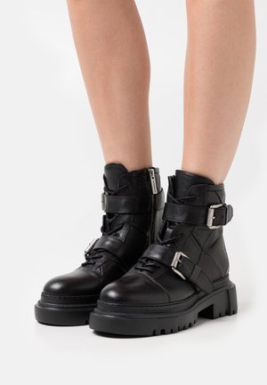 Bottines en cuir noir avec une semelle épaisse, dotées de plusieurs sangles, boucles et d'une fermeture éclair sur le côté. Texture lisse avec une finition mate.