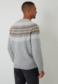 Grijze gebreide trui met een patronen yoke met zigzag- en diamantontwerpen in wit, bruin en donkerder grijs, voorzien van geribde manchetten en zoom.