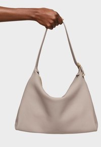 Beige leather handbag with a curved shape and textured finish. Features a single, adjustable strap and gold hardware accents.