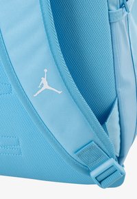 Light blue backpack made of textured fabric with a smooth strap. Features a white Jumpman logo and adjustable buckle detail.