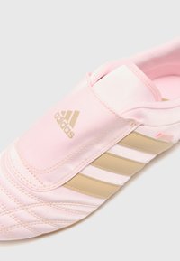 Sapatilha atlética rosa clara com acabamento em seda, apresentando detalhes em dourado e três riscas douradas. Parte superior suave e acolchoada para conforto.