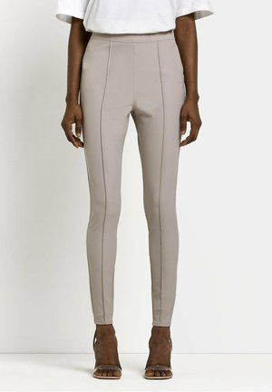 Dark-skinned person wearing fitted beige pants with front seams and high-waist, paired with open-toe heels and a white top.