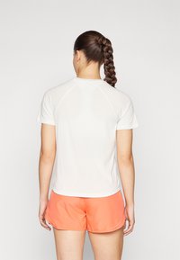 Camiseta atlética blanca de manga corta, con diseño sin costuras y cuello redondo. Combinada con pantalones cortos color coral, que muestran un ajuste relajado.