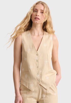 Beige Leinenweste mit V-Ausschnitt, vorderen Knöpfen und dekorativen weißen Mustern. Zwei Vordertaschen ergänzen das maßgeschneiderte Design.
