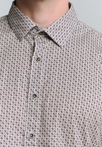 Kragenhemd aus gewebtem Stoff mit geometrischem Muster in Rosa, Grün und Weiß, mit Metallknöpfen und leichter Textur.