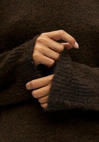 Pull en maille marron avec une finition texturée. Les manches sont longues et amples, avec un poignet côtelé qui s'étend au-delà des mains.