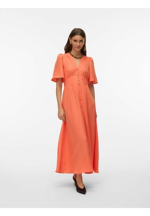 Kvinne iført en korallfarget button-up maxikjole med korte ermer, V-hals, brunt halskjede og svarte hæler mot en enkel hvit bakgrunn.