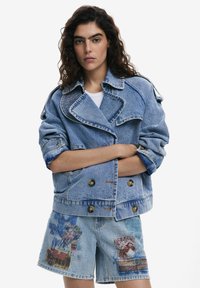 Sacou din denim de culoare albastru deschis, cu guler mare, design dublu cu nasturi aurii. Prezintă manșete supradimensionate și șorturi cu imprimeu grafic colorat.