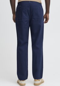 Pantaloni bleumarin din bumbac durabil, cu design cu picior drept, talie elastică și două buzunare în spate. Purtați cu pantofi bej.